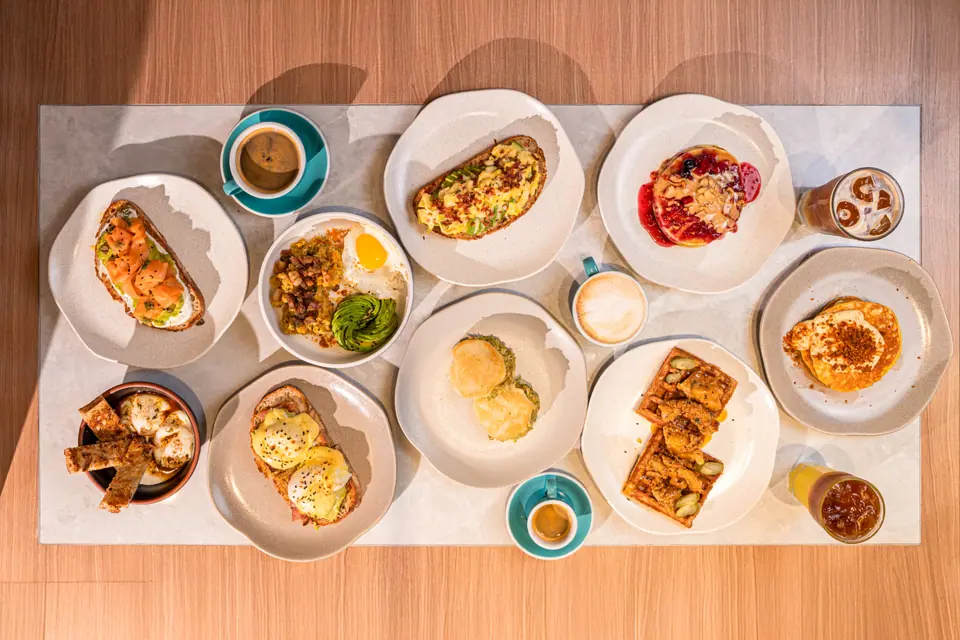 Mesa servida con desayunos de PROT INN vista desde arriba: huevos benedictinos, tostadas de salmón, waffles y café